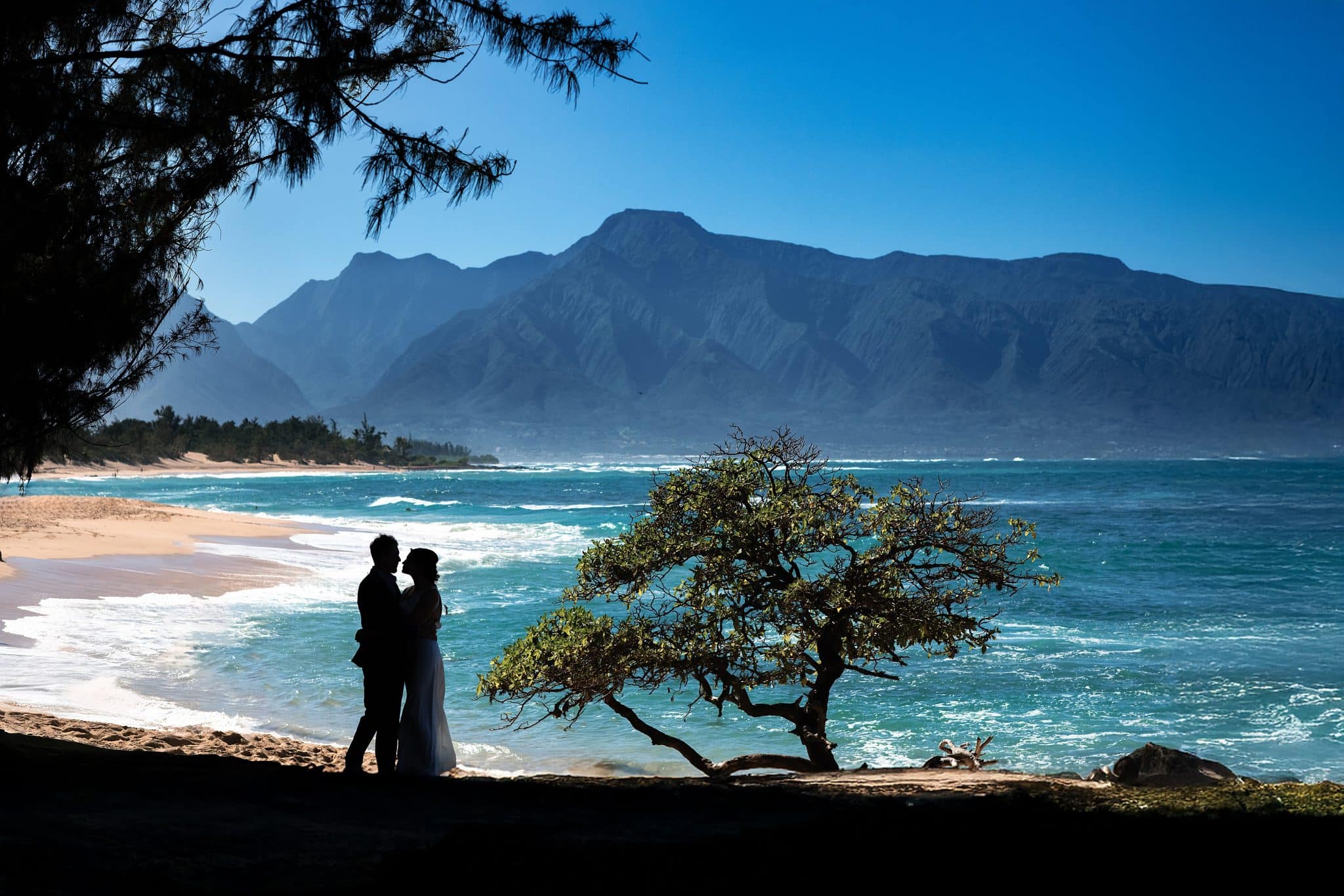 Cheryl and Lincoln's silhouette hugging with the blue ocean and mountains behind them