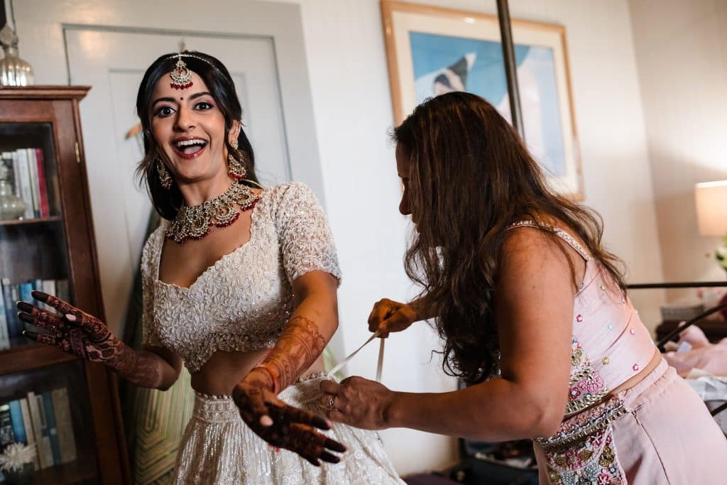 Indian-Wedding-in-Maui-_0002 - Ann Arbor Wedding Photographer The bride smiling at the camera while her mother ties her beaded skirt together.