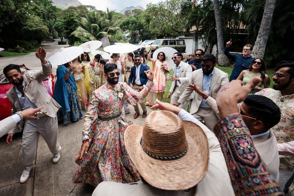 Indian-Wedding-in-Maui-_0013 - Ann Arbor Wedding Photographer Wedding guests circle the groom and celebrate in dance and chanting. Some guests are holding white parasaols.