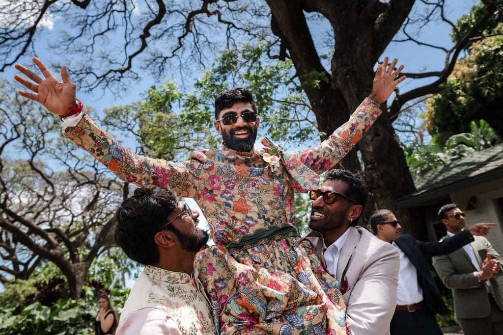 Indian-Wedding-in-Maui-_0015 - Ann Arbor Wedding Photographer A joyful groom wearing embroidered sherwani and holding his arms up as two men lift him into the air.