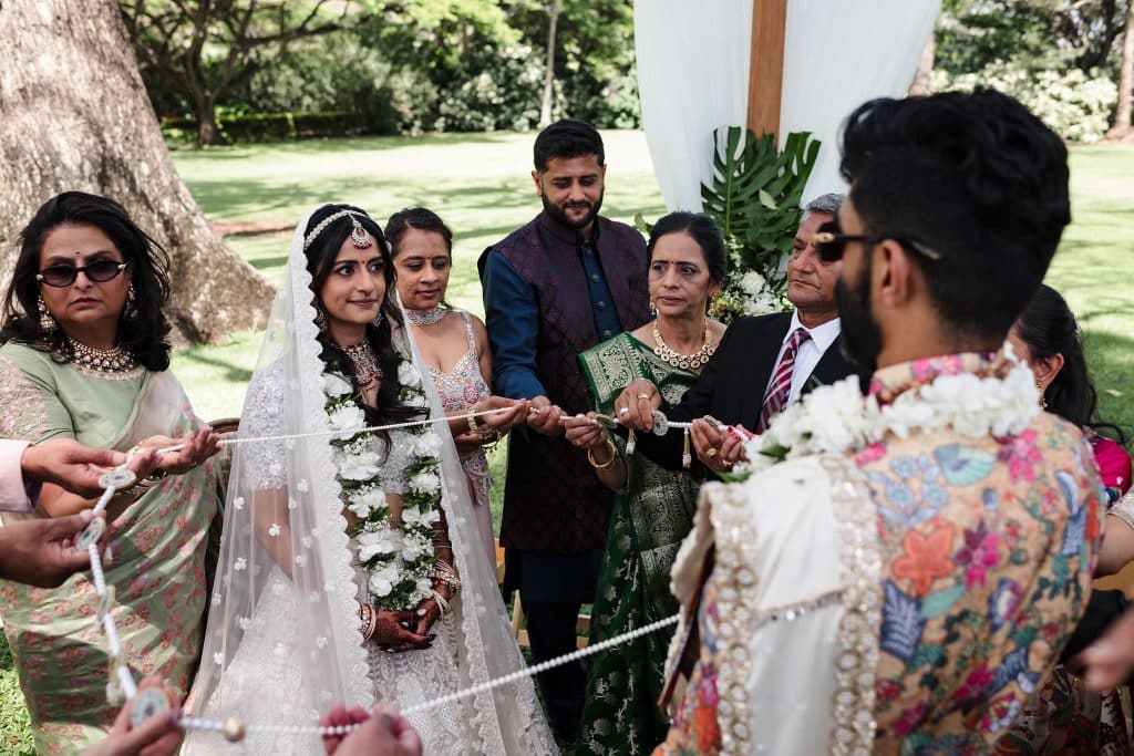 Indian-Wedding-in-Maui-_0019 - Ann Arbor Wedding Photographer Wedding ceremony where guests are between the bride and groom holding onto a beaded circle as the bride and groom unite.
