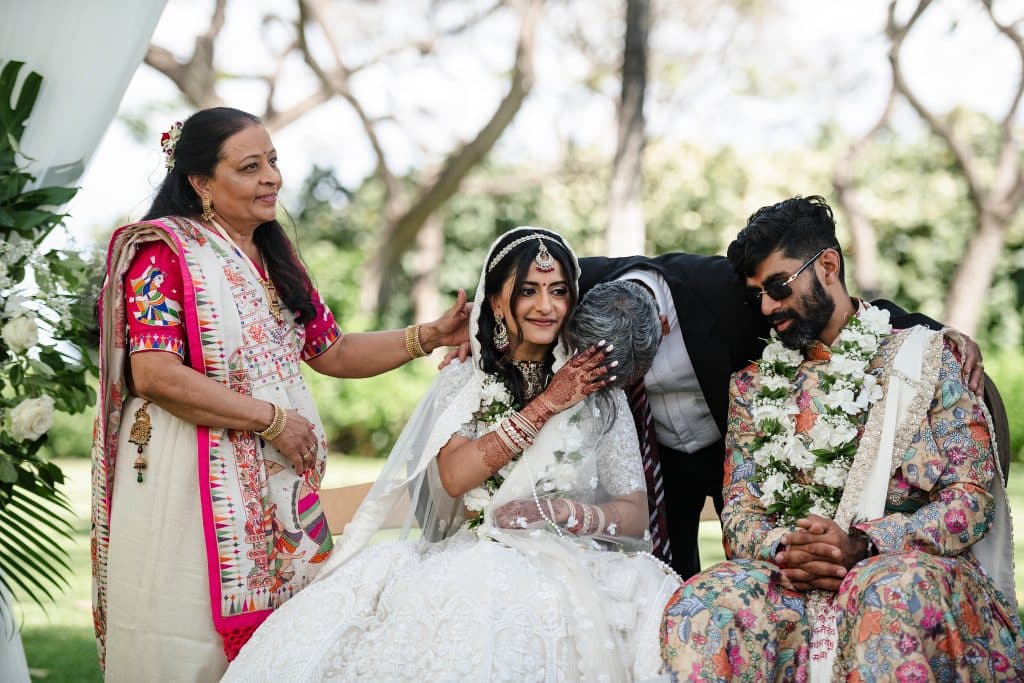 Indian-Wedding-in-Maui-_0020 - Ann Arbor Wedding Photographer A bride gently touching a mans head who is resting on her shoulder as he gives her and her husband a hug. A woman wearing pink is standing on the other side of the bride gently touching his hand on the brides shoulder.