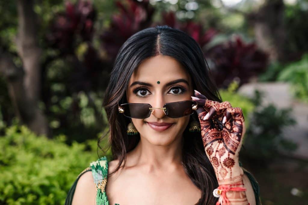 Indian-Wedding-in-Maui-_0029 - Ann Arbor Wedding Photographer A close up of a woman looking at the camera and pulling down her sunglasses with her hand that is covered in intricate henna designs.