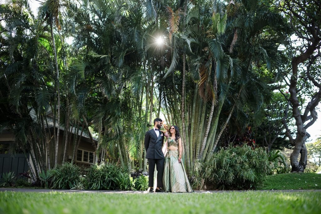 Indian-Wedding-in-Maui-_0031 - Ann Arbor Wedding Photographer Bride and groom standing in front of palm trees and laughing as she rests her arm on his shoulder. They're both wearing sunglasses.